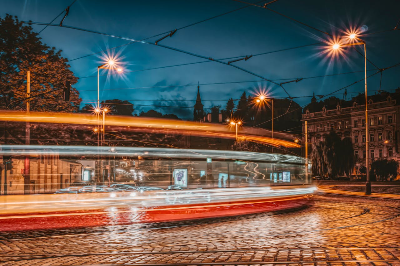 Vibrant urban scene with light streaks from moving tram on a cobblestone street at night.