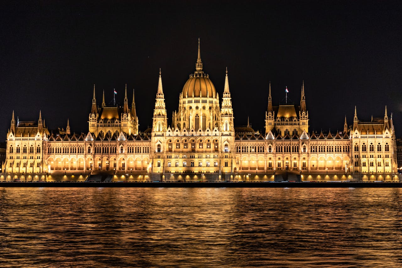 Illuminated Budapest Parliament Building reflecting over the Danube River at night.